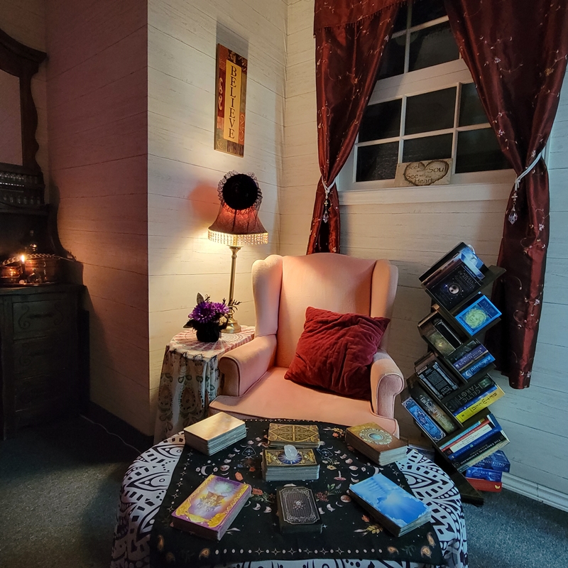 Reader’s chair beside a tarot table and leaning bookshelf filled with oracle decks in The Zen Shop’s Reading Parlour