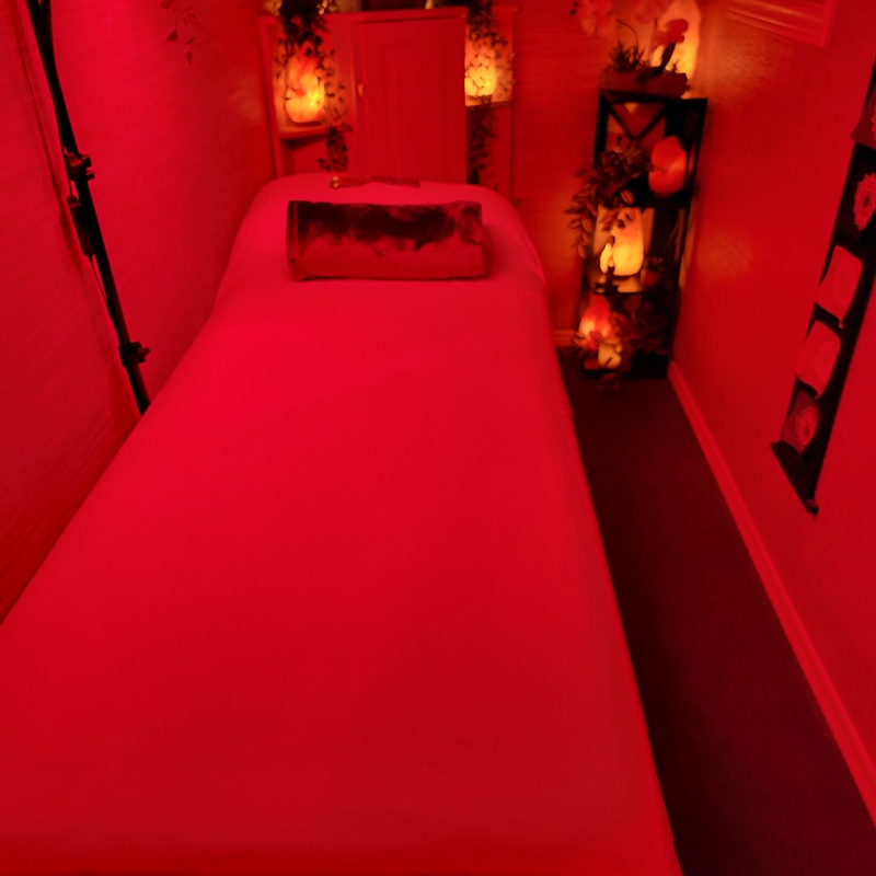 The Zen Shop Healing Room illuminated in red during a Red Light Therapy session, with Reiki bed, glowing salt lamps, chakra banner, and crystal shelves