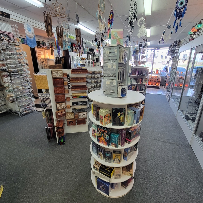 View from the back south corner of The Zen Shop Oshawa looking toward the centre aisle, featuring incense, carved wooden boxes, tarot and oracle cards, and ceiling-hung dreamcatchers and wind chimes in a warmly lit metaphysical setting.